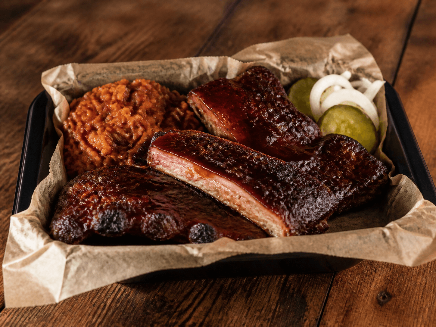 Smoked rib plate with sauced ribs, a side, pickles, and onions.